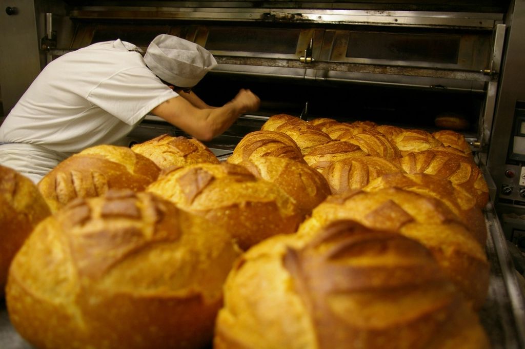 Baker taking golden loaves from the oven